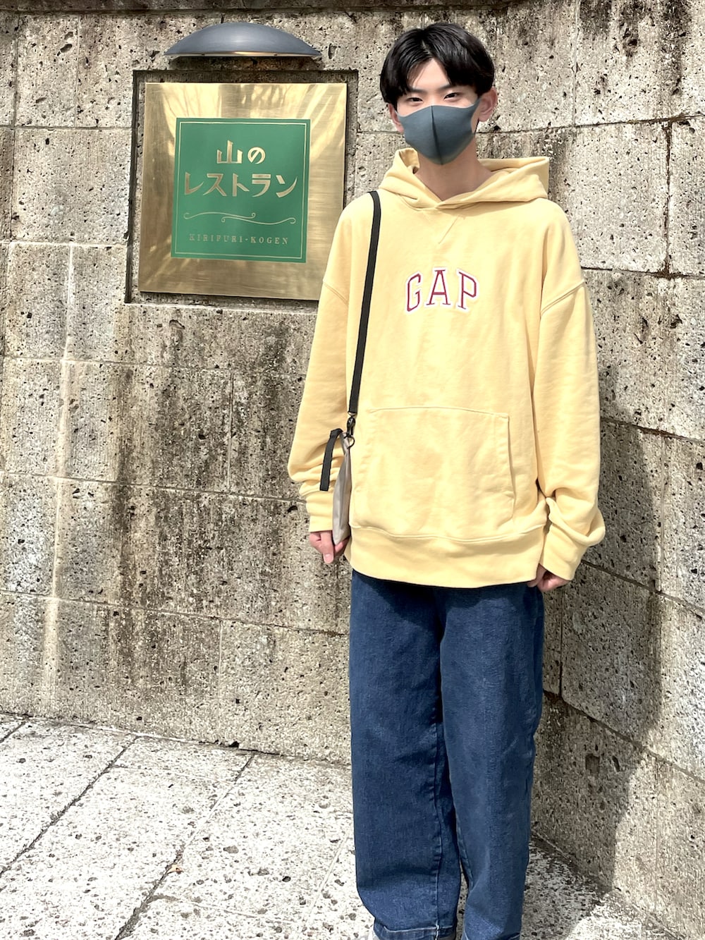 イエロー系のパーカー、ベージュ系のショルダーバッグ、ブルー系のデニムパンツを着用したメンズの春コーディネートの3枚目の写真