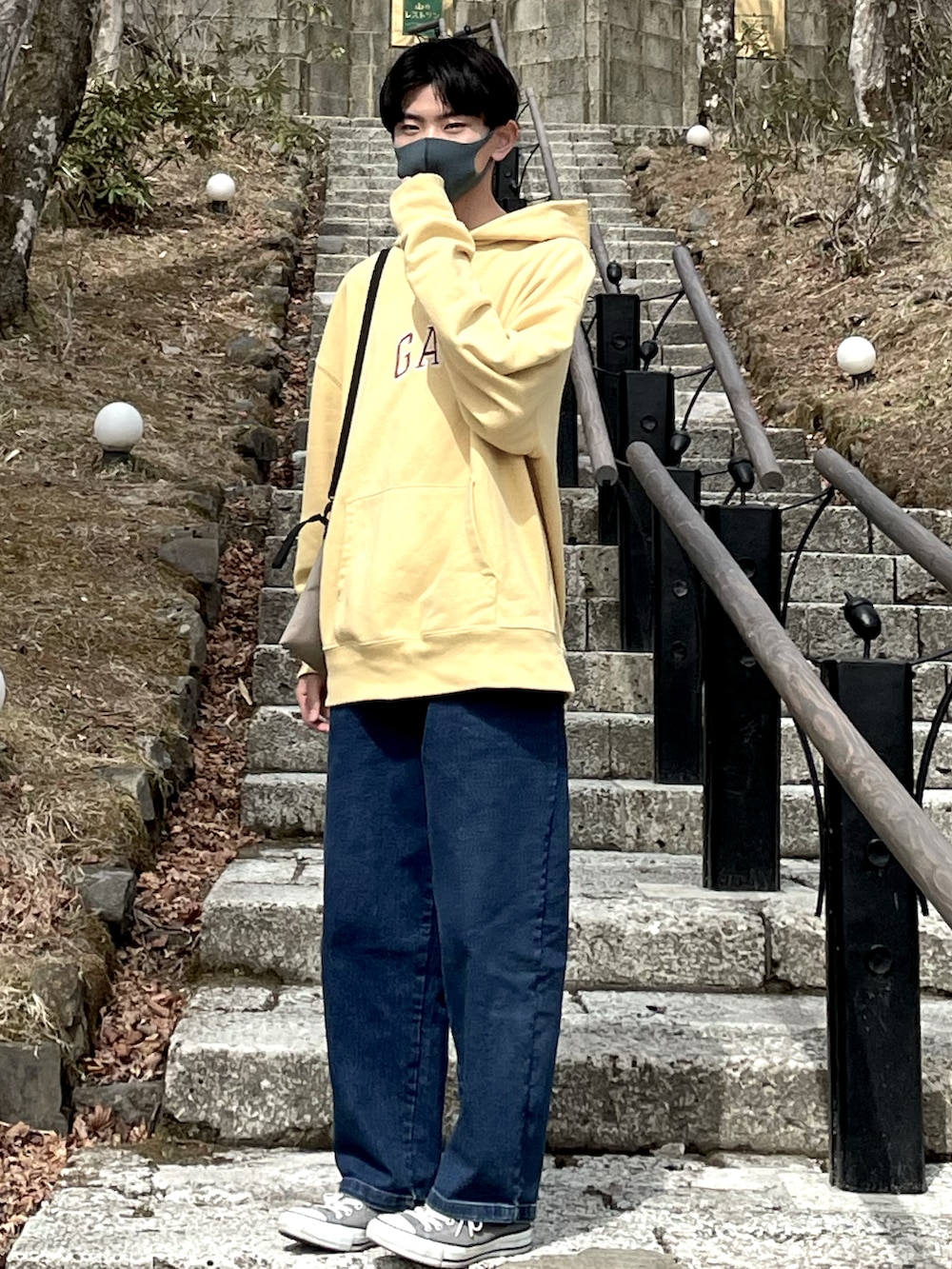 イエロー系のパーカー、ベージュ系のショルダーバッグ、ブルー系のデニムパンツを着用したメンズの春コーディネートの2枚目の写真