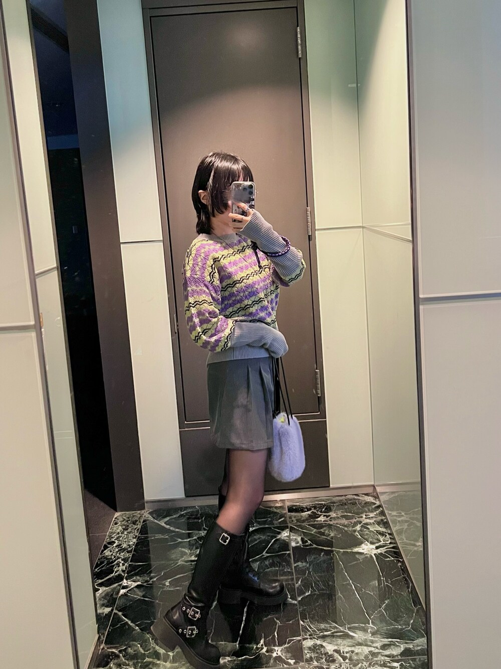 パープル系のバッグ、ブルー系のニット/セーター、ブラック系のブーツを着用したレディースの冬コーディネートの2枚目の写真