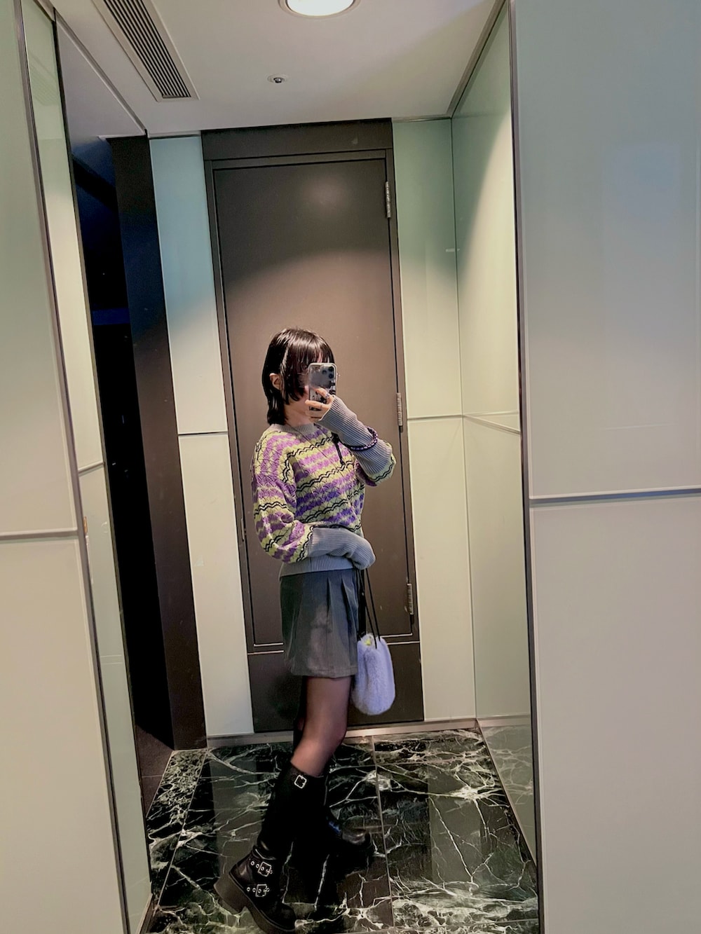 パープル系のバッグ、ブルー系のニット/セーター、ブラック系のブーツを着用したレディースの冬コーディネートの3枚目の写真