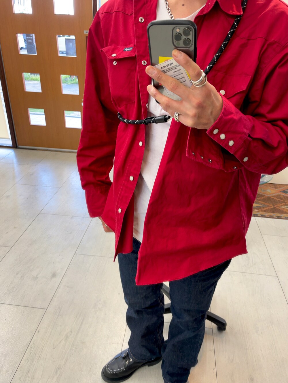 ブラック系のブーツ、ブルー系のデニムパンツ、レッド系のミリタリージャケットを着用したメンズの春コーディネートの2枚目の写真