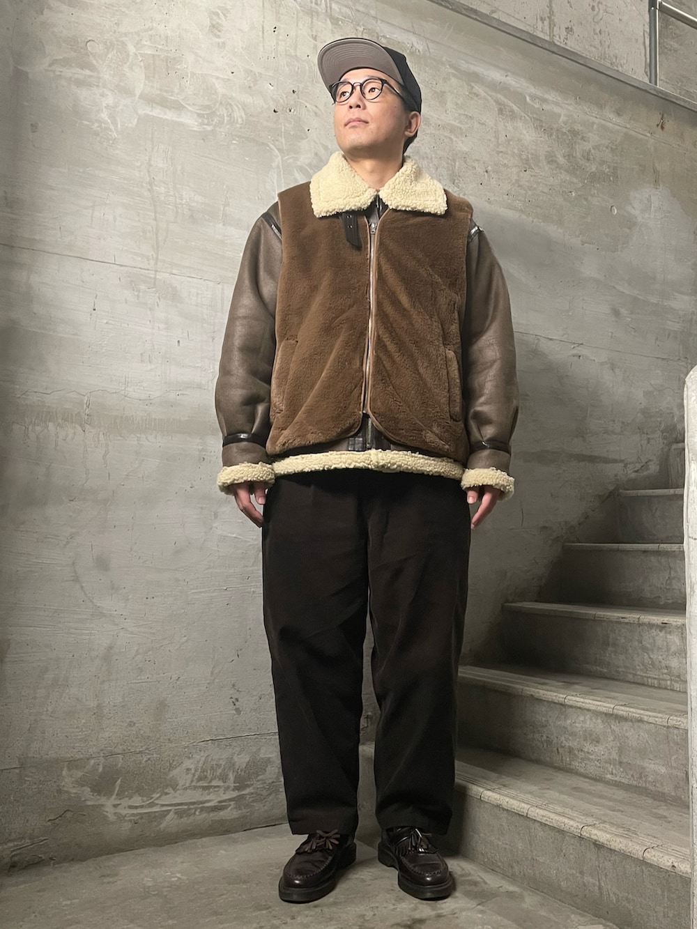 ブラウン系のムートンコート、ブラウン系のベスト、ブラウン系のその他パンツを着用したメンズの冬コーディネートの2枚目の写真