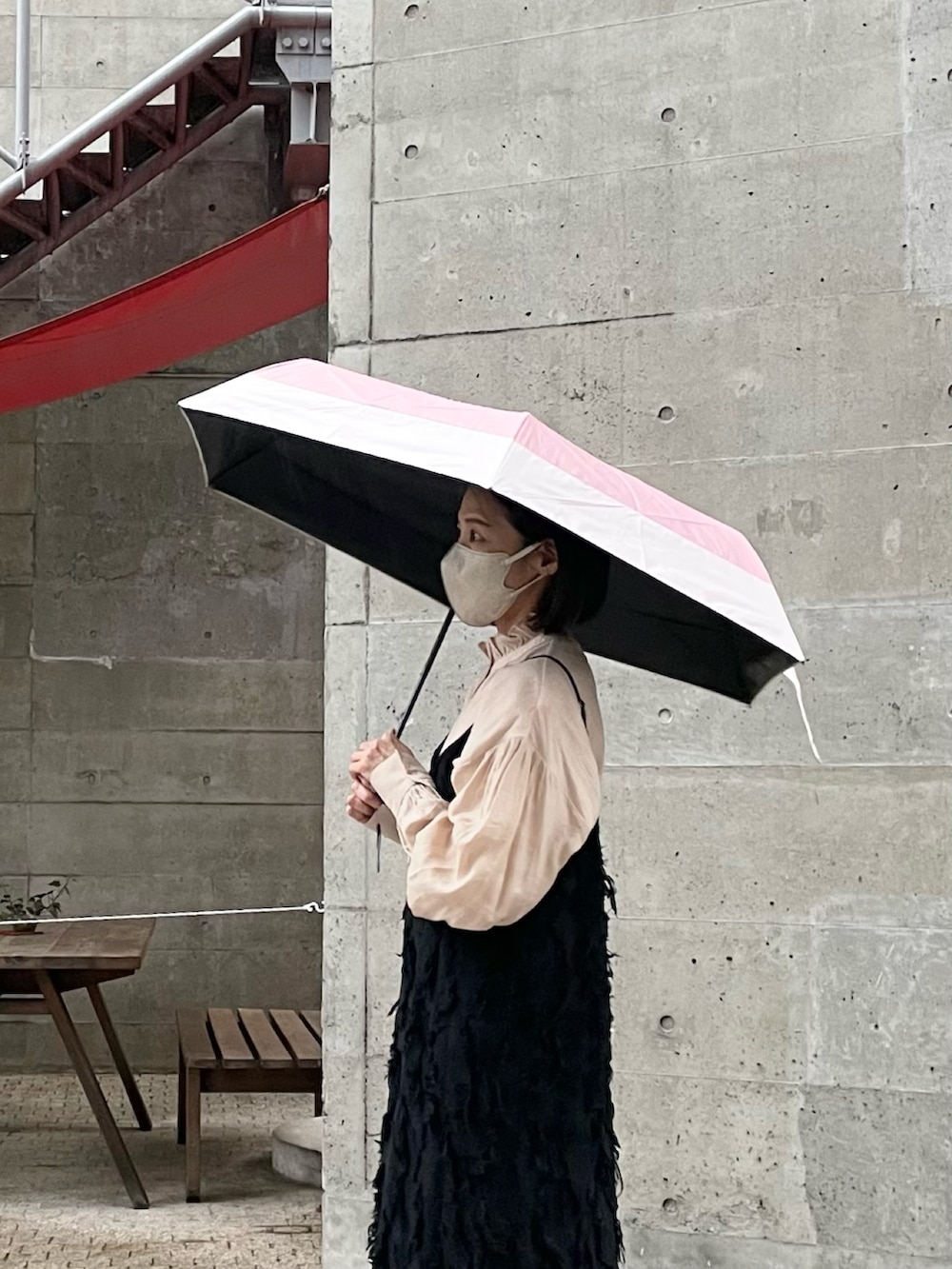 ブラック系のワンピース、ベージュ系のシャツ/ブラウス、ピンク系の折りたたみ傘を着用したレディースの春コーディネートの2枚目の写真