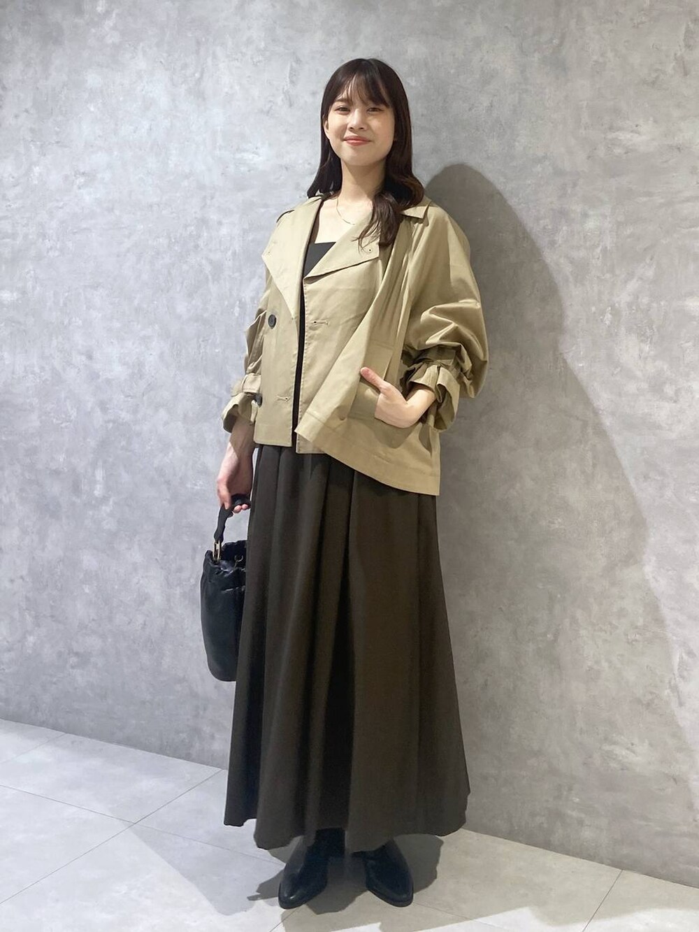 ブラウン系のジャンパースカート、ブラック系のショルダーバッグ、ベージュ系のトレンチコートを着用したレディースの秋コーディネートの3枚目の写真