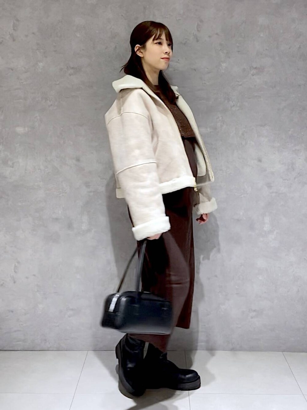 ブラウン系のワンピース、ブラック系のブーツ、ホワイト系のブルゾンを着用したレディースの冬コーディネートの2枚目の写真