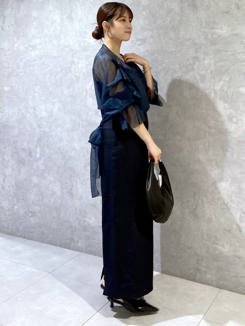 ブラック系のハンドバッグ、ブラック系のパンプス、ブルー系のドレスを着用したレディースの秋コーディネートの4枚目の写真