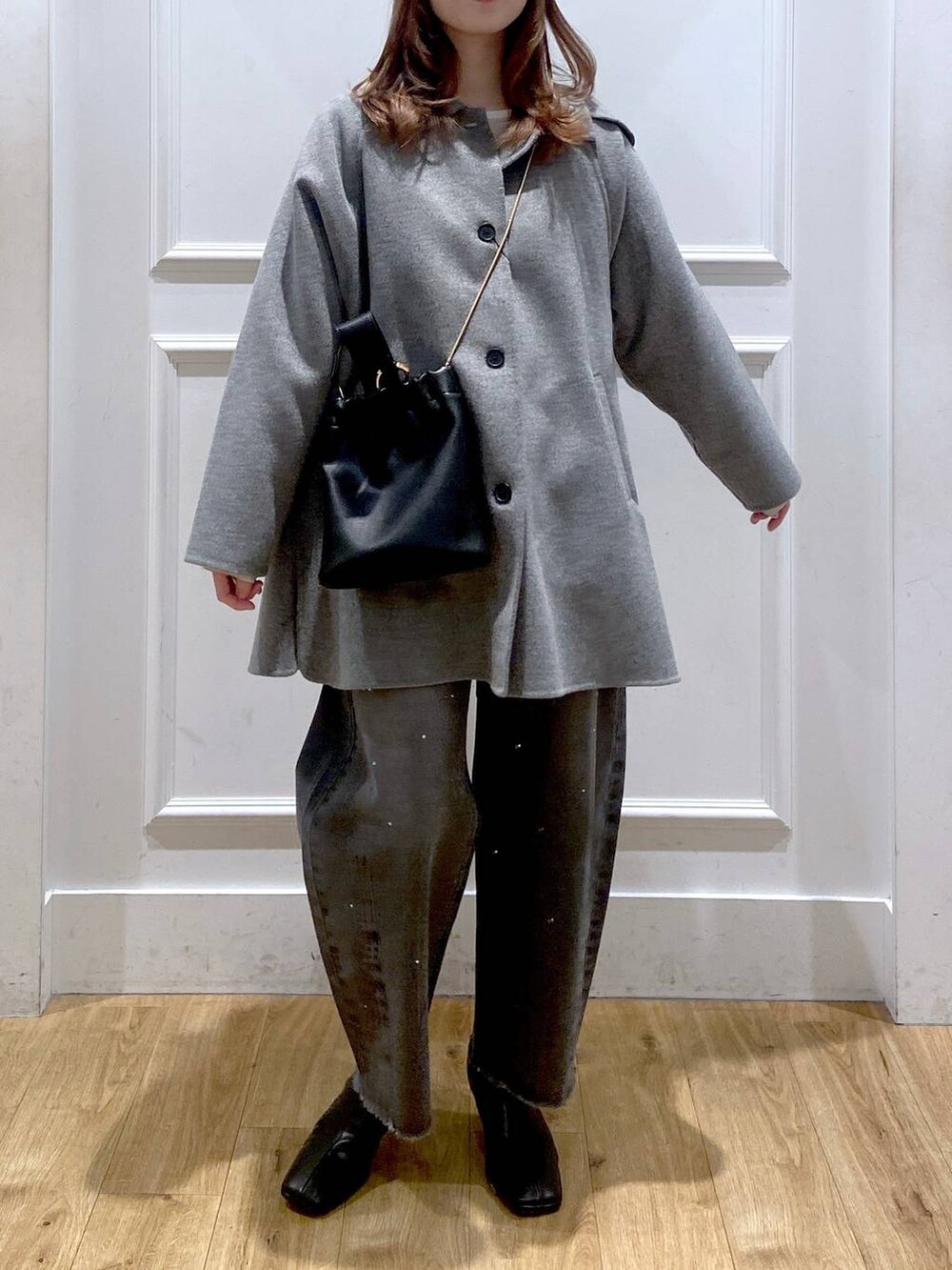 グレー系のステンカラーコート、ブラック系のブーツ、ホワイト系のTシャツ/カットソーを着用したレディースの冬コーディネートの2枚目の写真