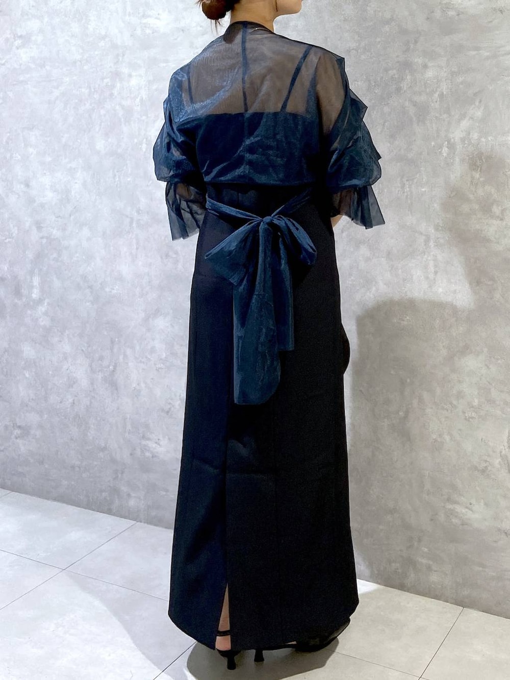 ブラック系のハンドバッグ、ブラック系のパンプス、ブルー系のドレスを着用したレディースの秋コーディネートの5枚目の写真