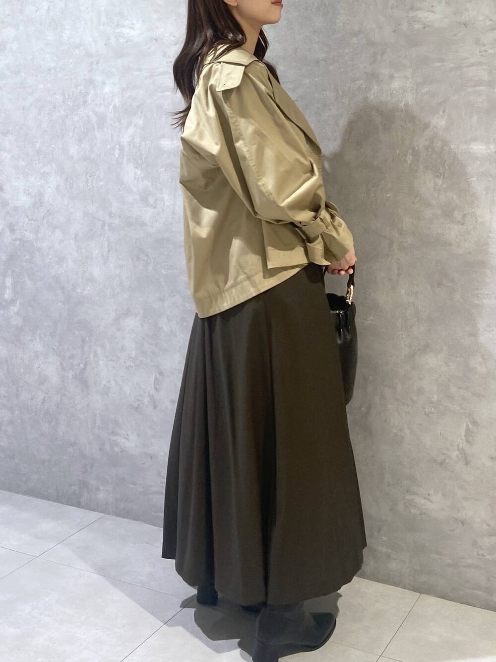 ブラウン系のジャンパースカート、ブラック系のショルダーバッグ、ベージュ系のトレンチコートを着用したレディースの秋コーディネートの5枚目の写真