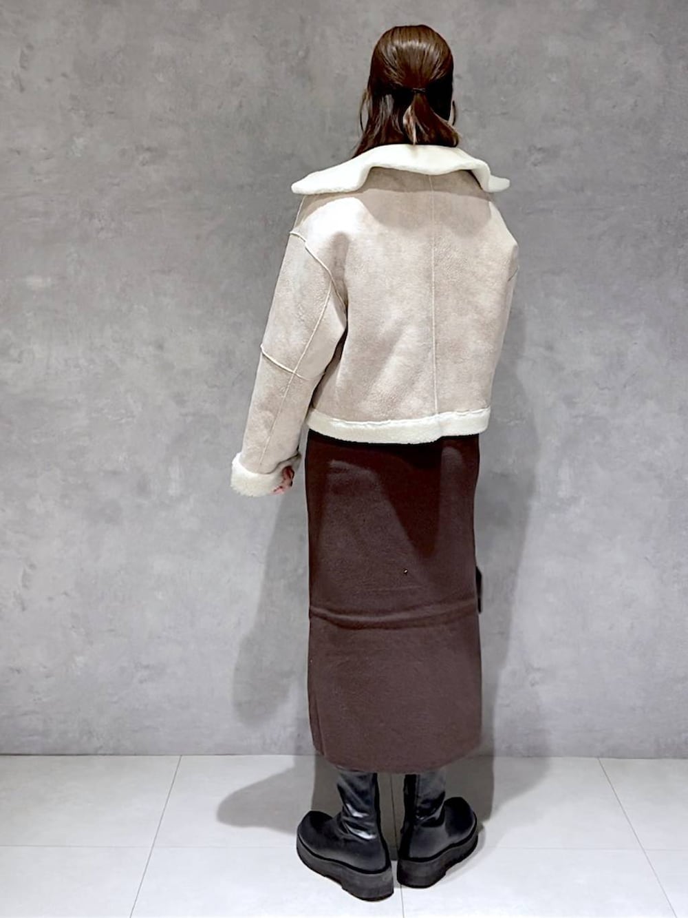 ブラウン系のワンピース、ブラック系のブーツ、ホワイト系のブルゾンを着用したレディースの冬コーディネートの3枚目の写真