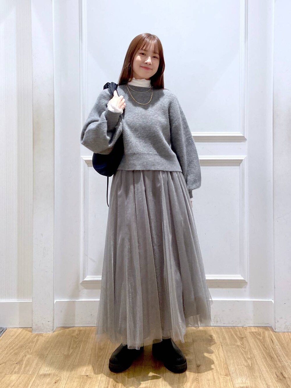 ホワイト系のTシャツ/カットソー、グレー系のカーディガン/ボレロ、ブラック系のブーツを着用したレディースの冬コーディネートの2枚目の写真