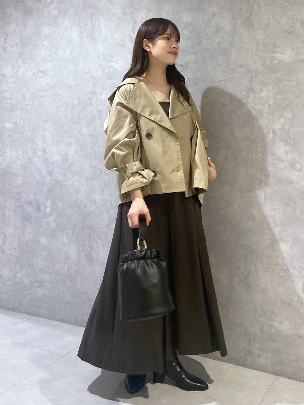 ブラウン系のジャンパースカート、ブラック系のショルダーバッグ、ベージュ系のトレンチコートを着用したレディースの秋コーディネートの4枚目の写真