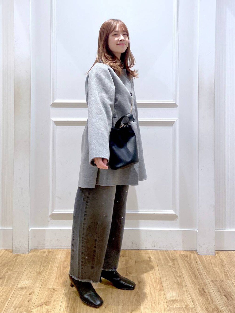 グレー系のステンカラーコート、ブラック系のブーツ、ホワイト系のTシャツ/カットソーを着用したレディースの冬コーディネートの3枚目の写真