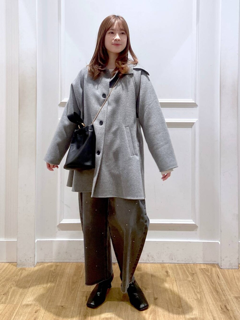 グレー系のステンカラーコート、ブラック系のブーツ、ホワイト系のTシャツ/カットソーを着用したレディースの冬コーディネートの6枚目の写真