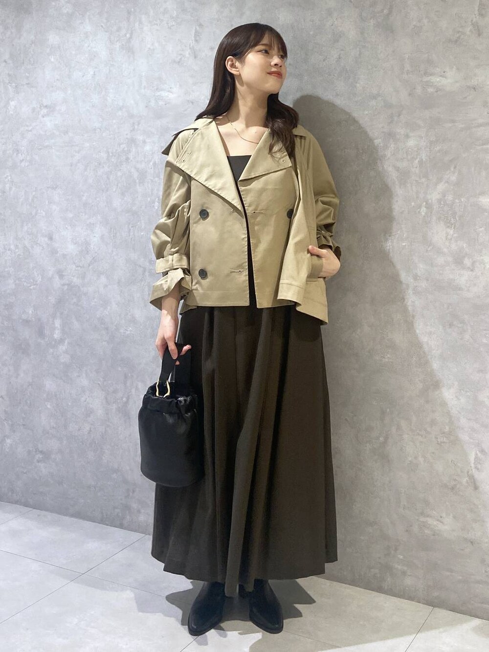 ブラウン系のジャンパースカート、ブラック系のショルダーバッグ、ベージュ系のトレンチコートを着用したレディースの秋コーディネートの2枚目の写真