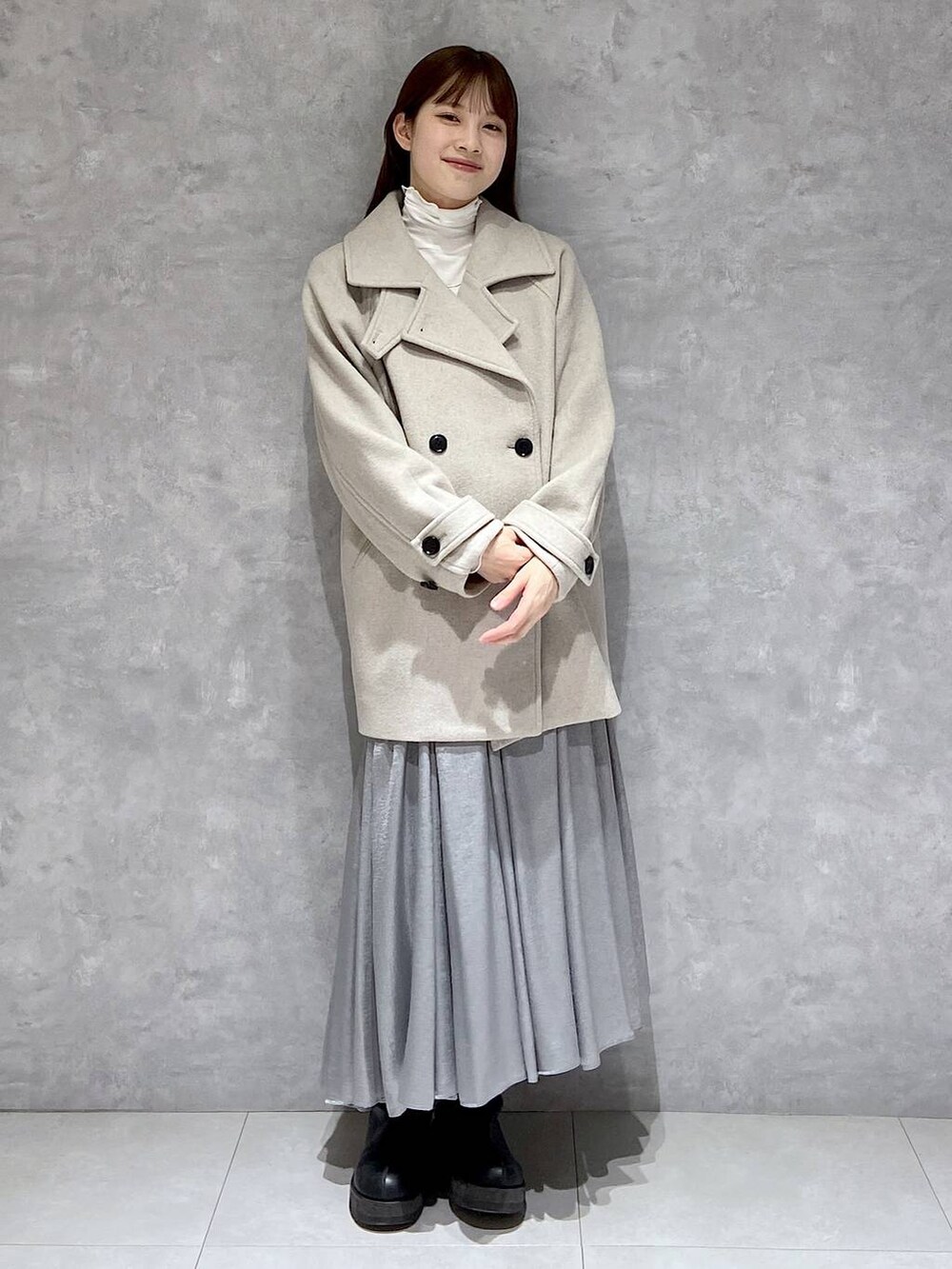 ベージュ系のピーコート、ホワイト系のTシャツ/カットソー、ブラック系のブーツを着用したレディースの冬コーディネートの2枚目の写真