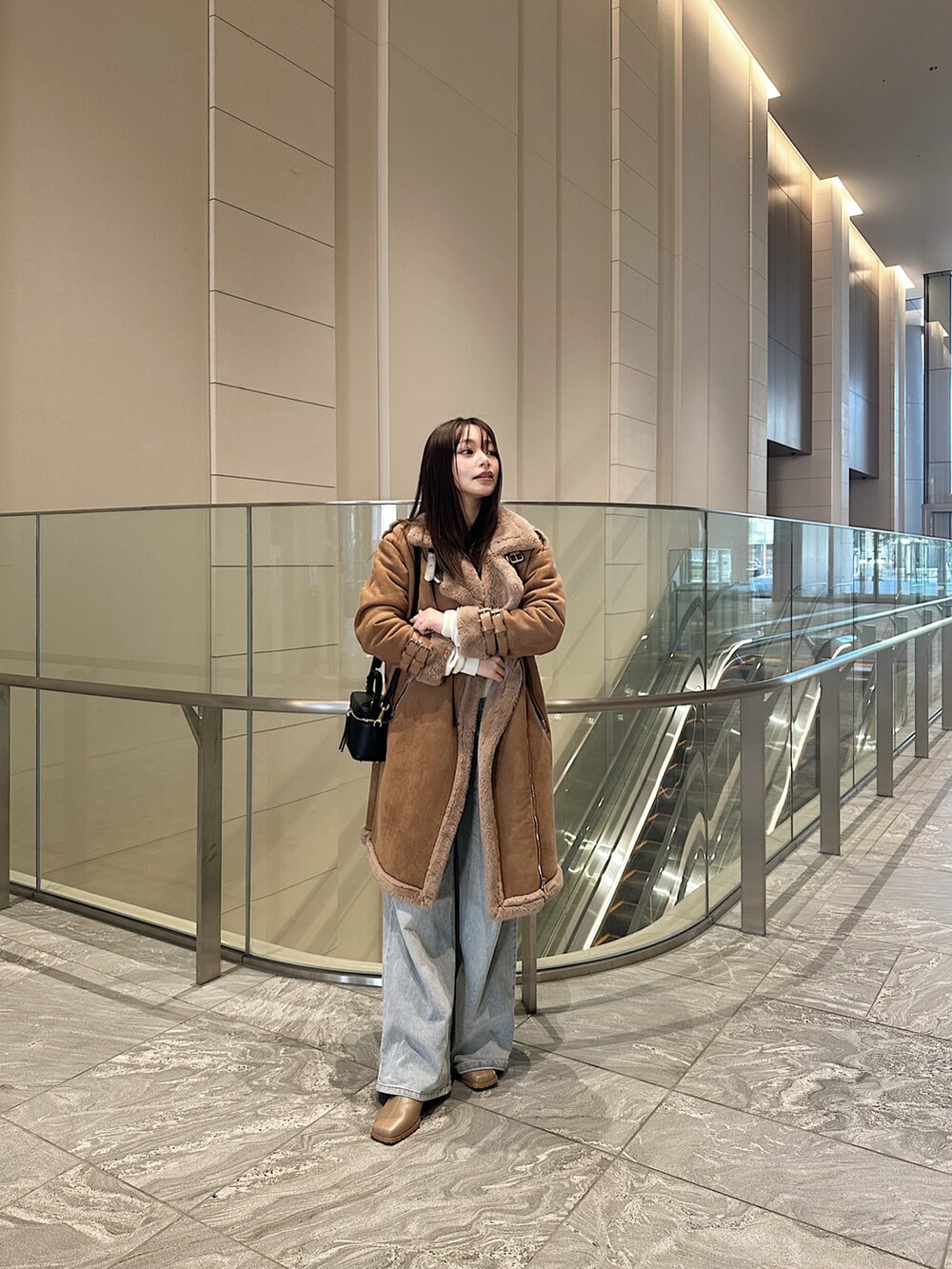 ブラウン系のジャケット/アウター、ブラック系のショルダーバッグ、ブルー系のデニムパンツを着用したレディースの冬コーディネートの2枚目の写真