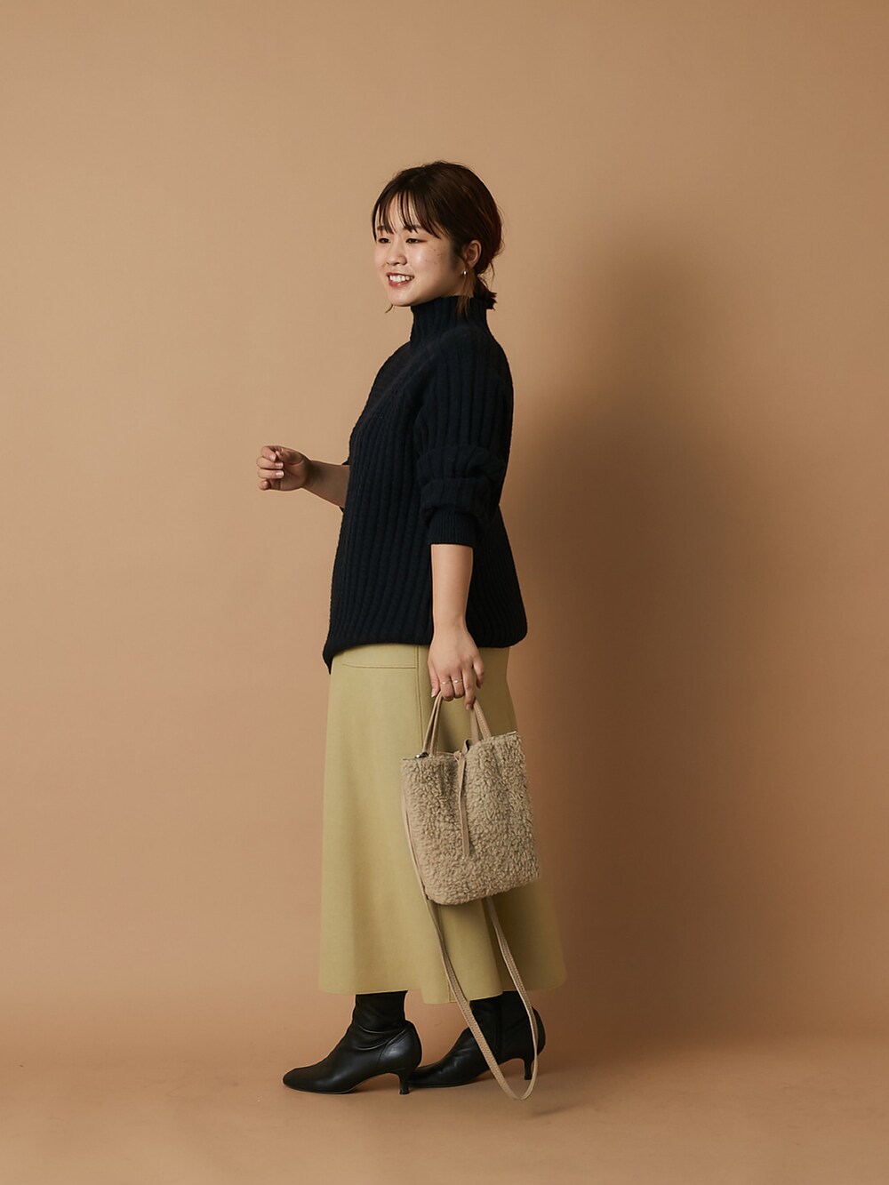 ベージュ系のショルダーバッグ、ブラック系のニット/セーター、イエロー系のスカートを着用したレディースの冬コーディネートの2枚目の写真