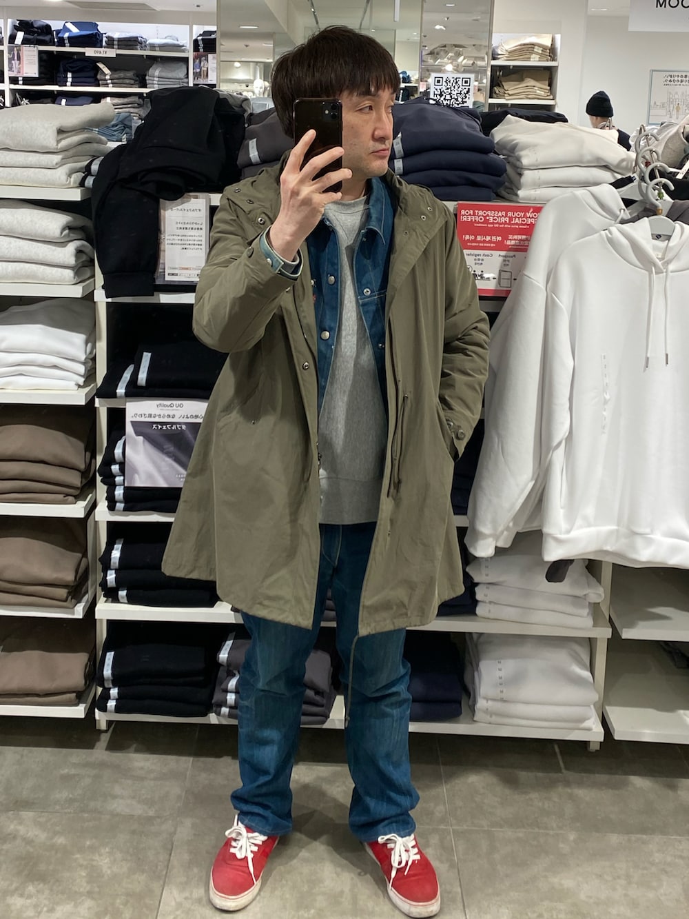 グリーン系のモッズコート、ブルー系のデニムパンツ、レッド系のスニーカーを着用したメンズの春コーディネートの3枚目の写真