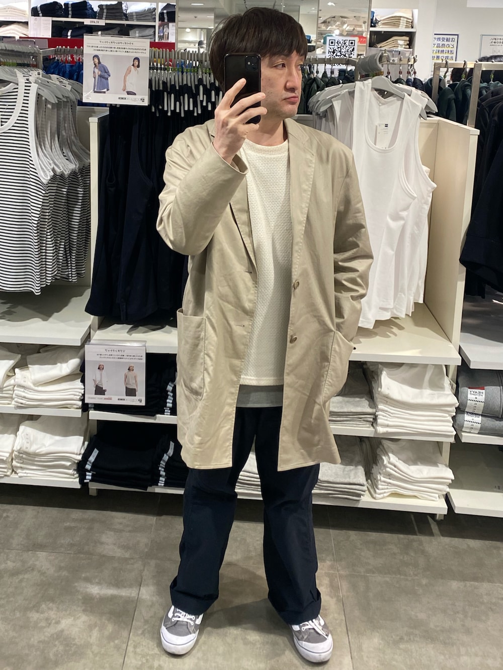 ベージュ系のチェスターコート、ブラック系のチノパンツ、グレー系のスニーカーを着用したメンズの春コーディネートの3枚目の写真