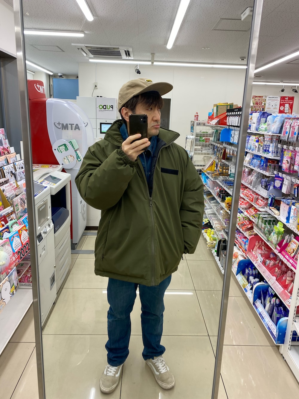 グレー系のカバーオール、ブルー系のデニムパンツ、ベージュ系のスニーカーを着用したメンズの冬コーディネートの2枚目の写真