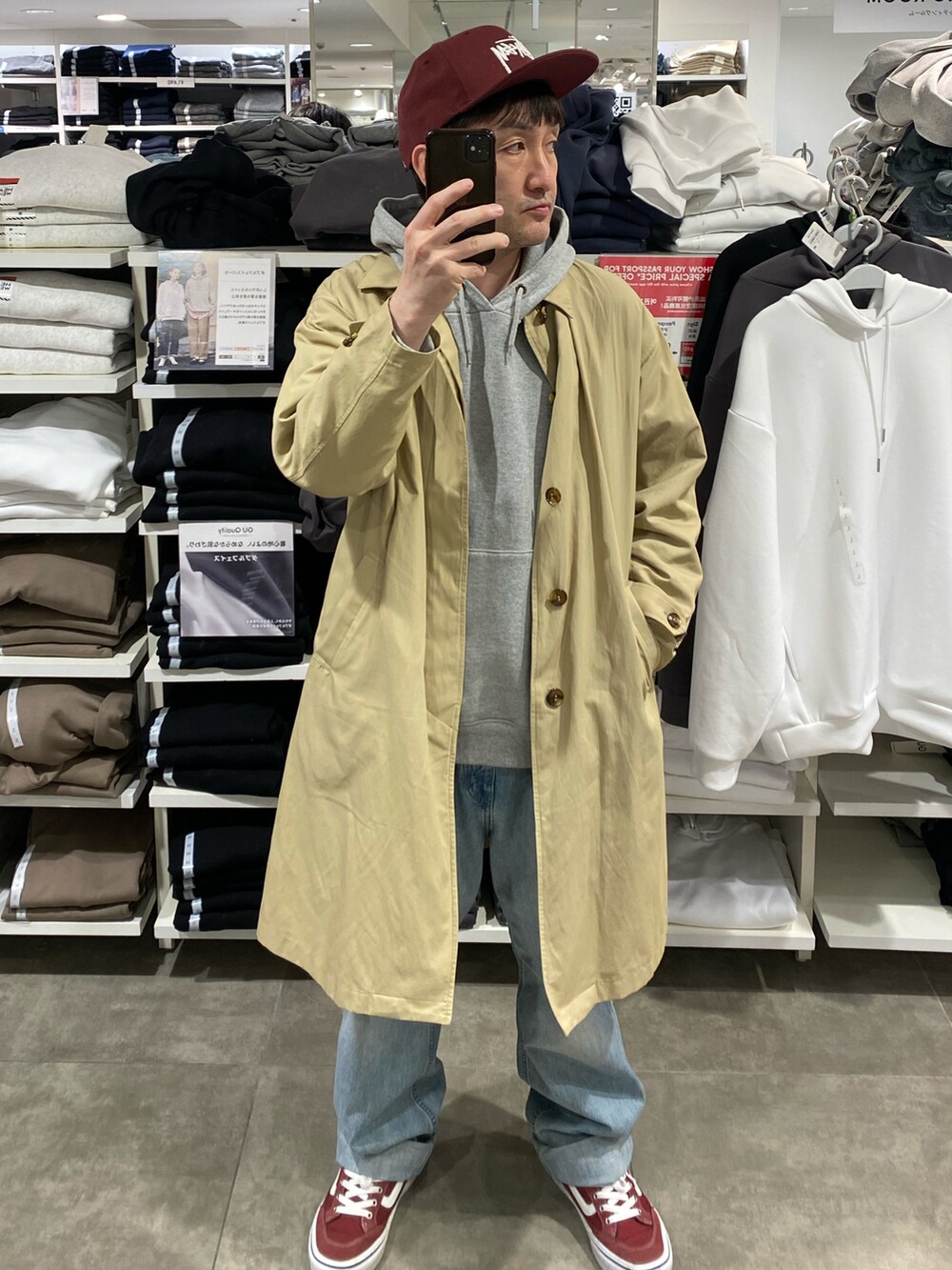 ベージュ系のステンカラーコート、ブルー系のデニムパンツ、レッド系のスニーカーを着用したメンズの春コーディネートの2枚目の写真