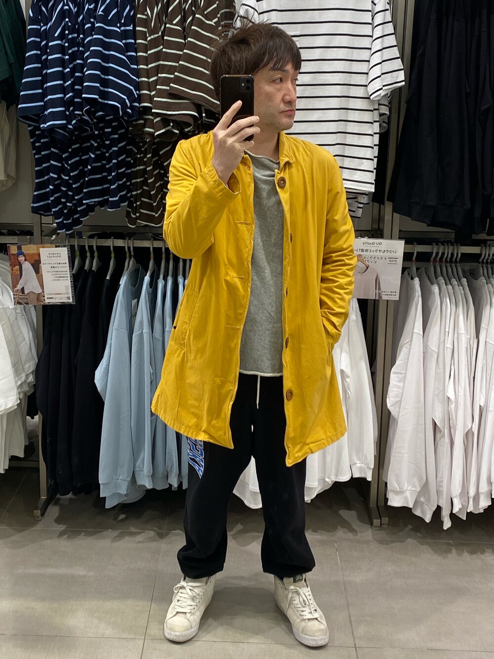 イエロー系のステンカラーコート、ブラック系のスウェットパンツ、ホワイト系のスニーカーを着用したメンズの春コーディネートの3枚目の写真