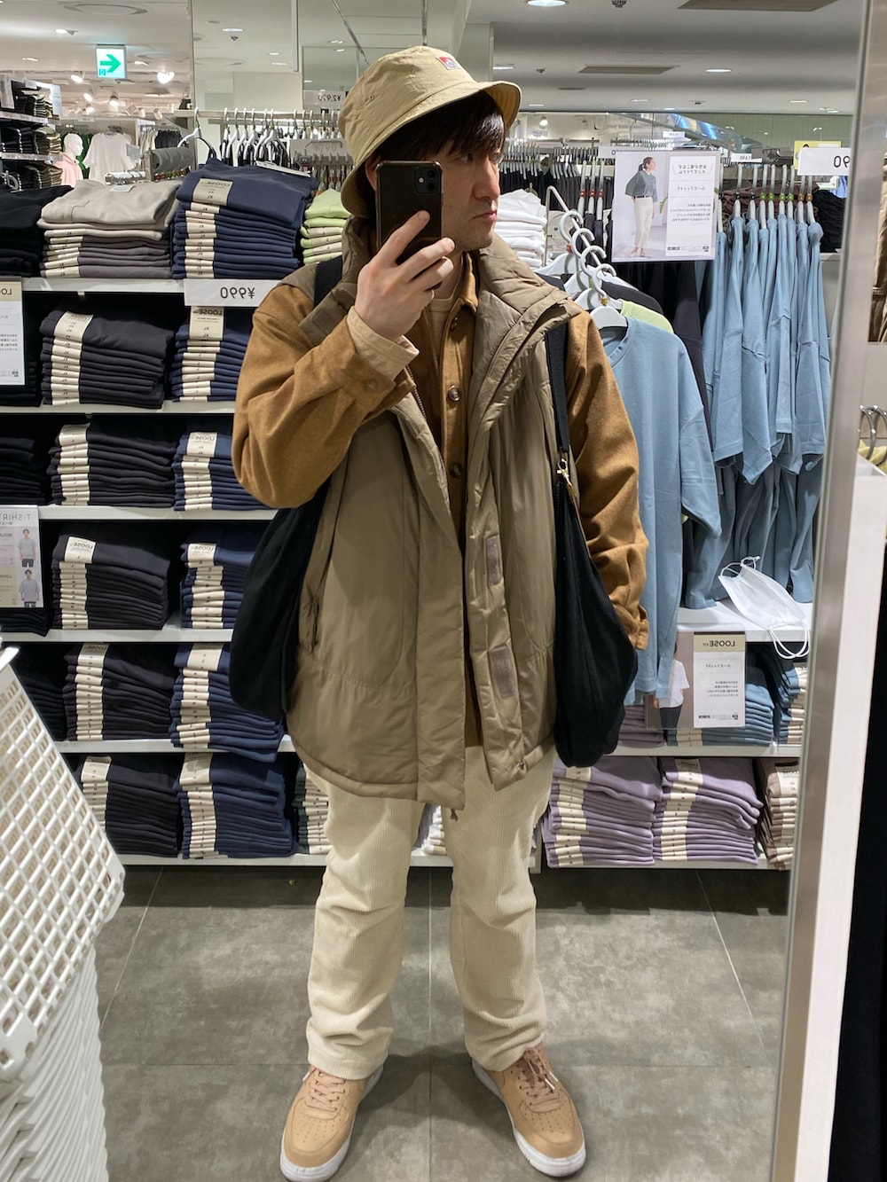 ブラック系のショルダーバッグ、イエロー系のカバーオール、ブラウン系のダウンベストを着用したメンズの春コーディネートの4枚目の写真