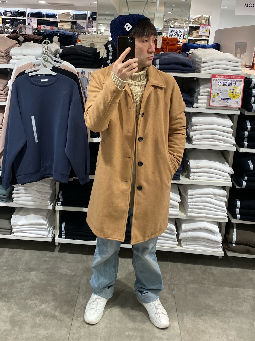 ベージュ系のステンカラーコート、ブルー系のデニムパンツ、ホワイト系のスニーカーを着用したメンズの冬コーディネートの2枚目の写真