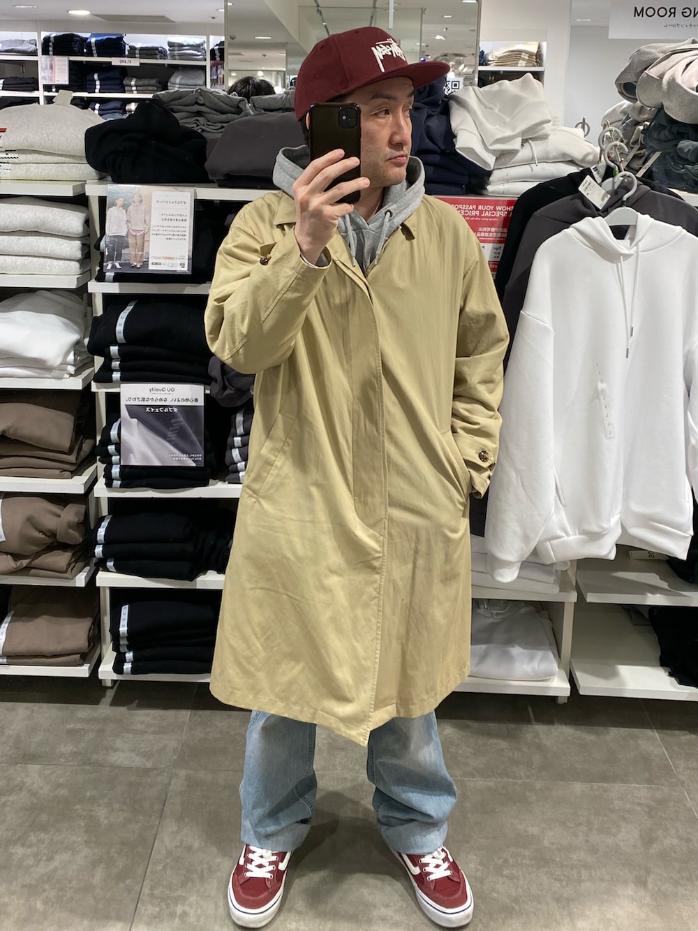 ベージュ系のステンカラーコート、ブルー系のデニムパンツ、レッド系のスニーカーを着用したメンズの春コーディネートの4枚目の写真