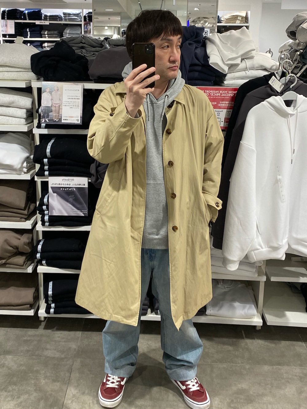 ベージュ系のステンカラーコート、ブルー系のデニムパンツ、レッド系のスニーカーを着用したメンズの春コーディネートの3枚目の写真