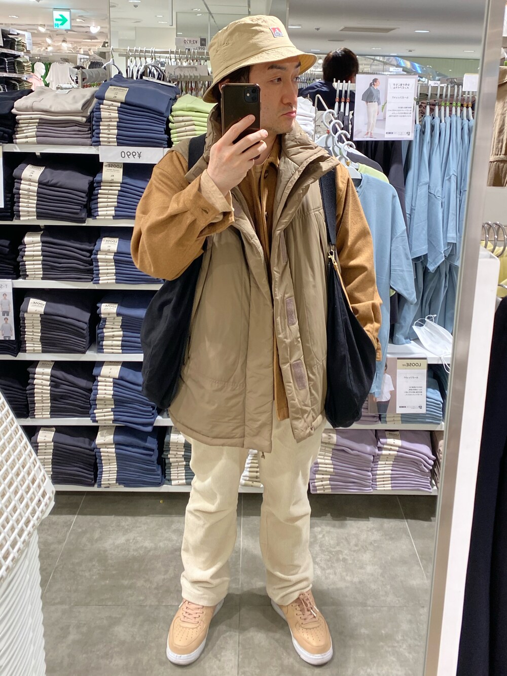 ブラック系のショルダーバッグ、イエロー系のカバーオール、ブラウン系のダウンベストを着用したメンズの春コーディネートの3枚目の写真