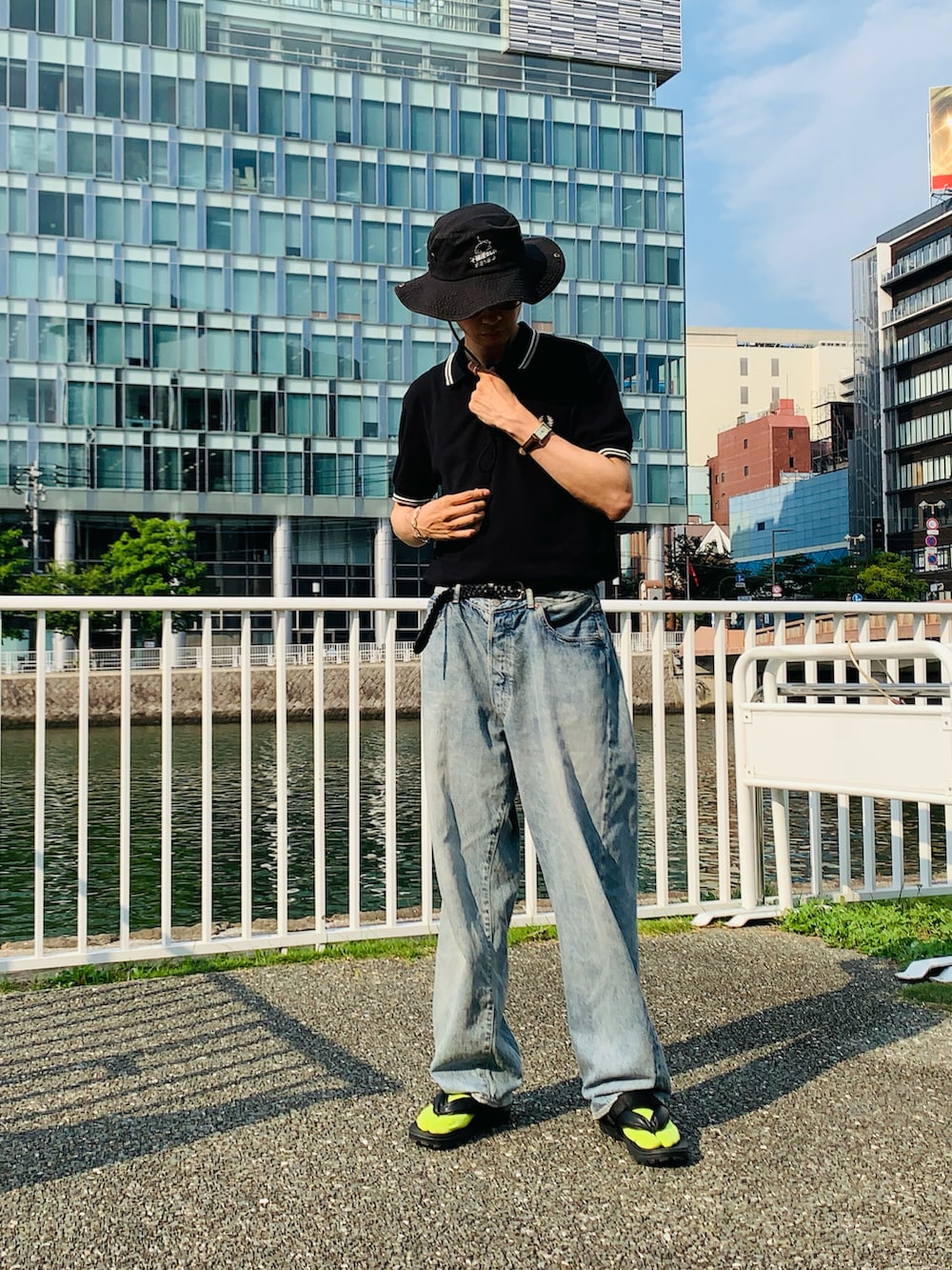 ブラック系のポロシャツ、ブルー系のデニムパンツ、ブラック系のサンダルを着用したメンズの夏コーディネートの2枚目の写真