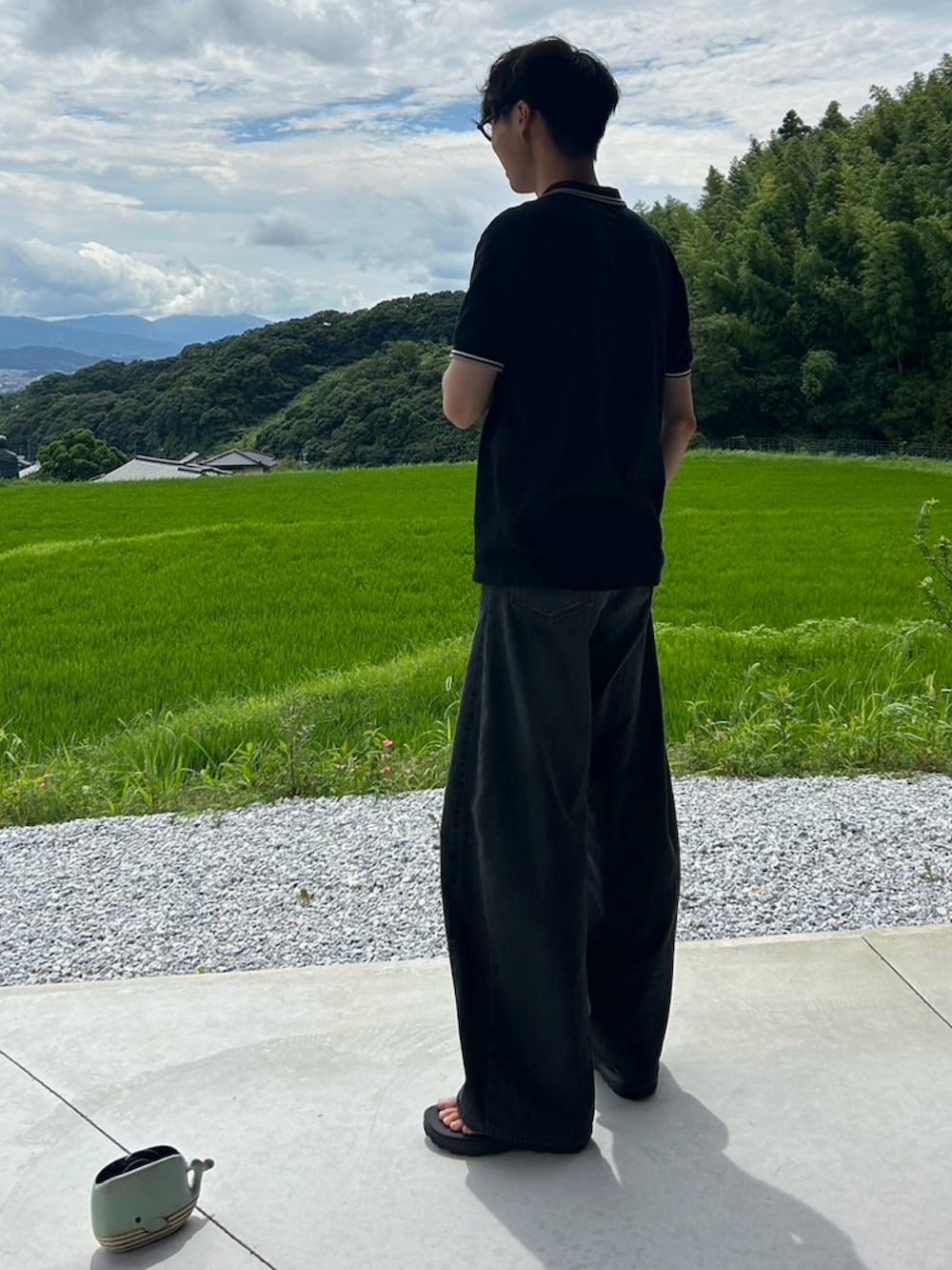 ブラック系のポロシャツ、ブラック系のデニムパンツ、ブラック系のサンダルを着用したメンズの夏コーディネートの2枚目の写真