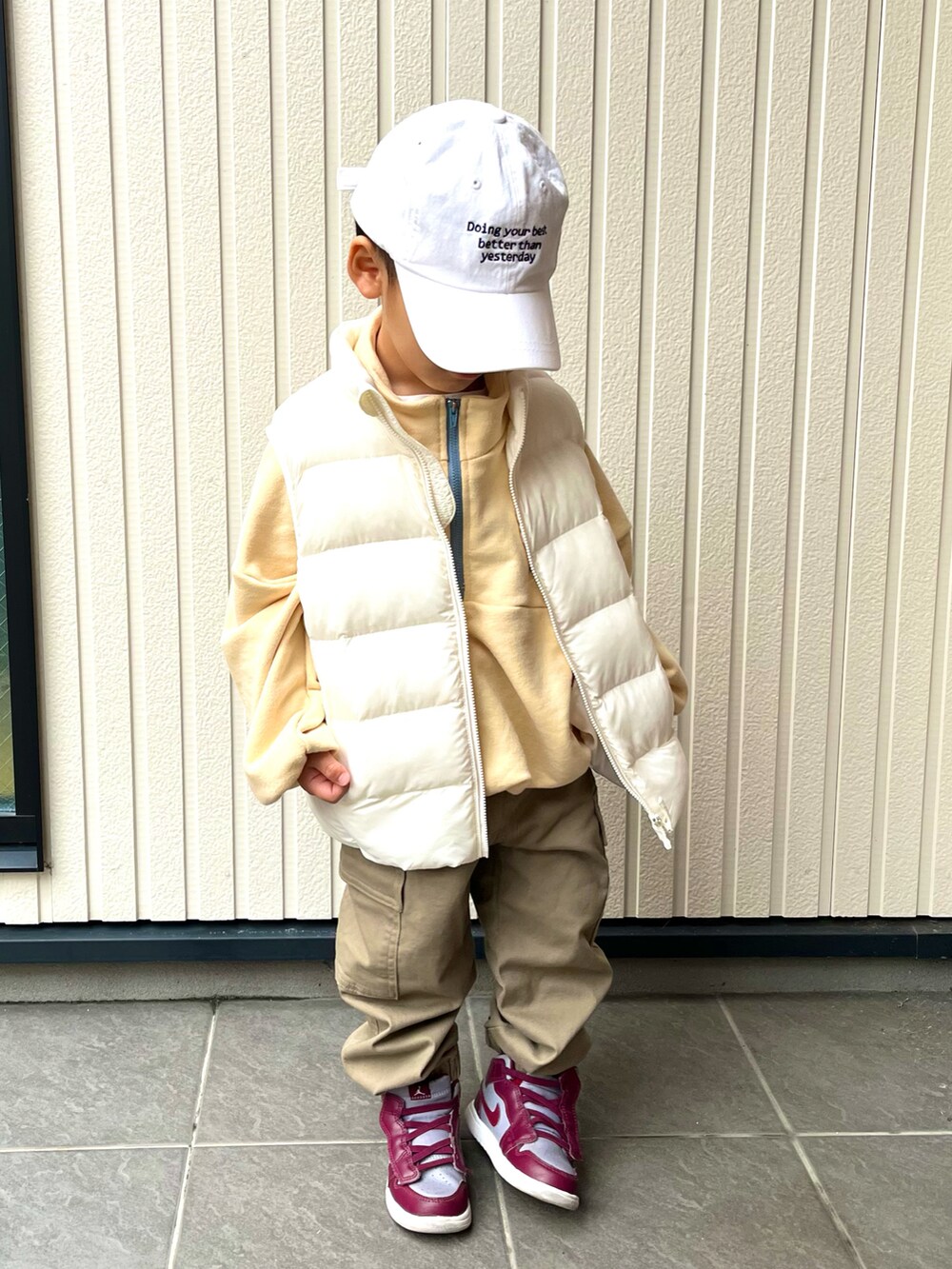 イエロー系のトップス、ベージュ系のカーゴパンツ、ホワイト系のダウンベストを着用したキッズの冬コーディネートの2枚目の写真