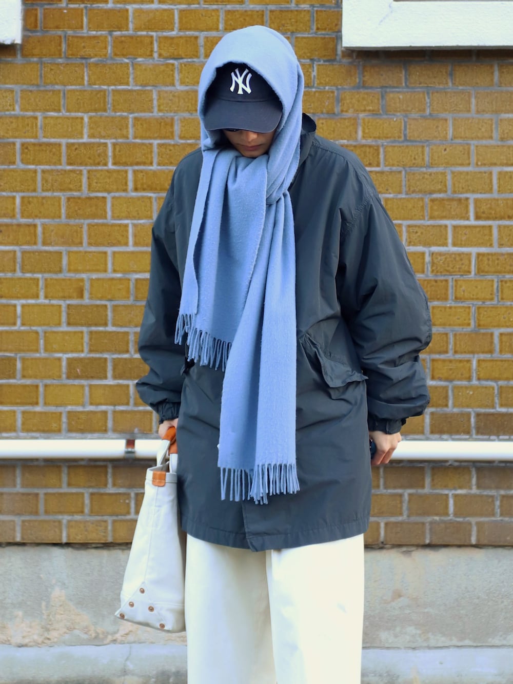 グレー系のモッズコート、ベージュ系のハンドバッグ、ホワイト系のチノパンツを着用したメンズの冬コーディネートの3枚目の写真