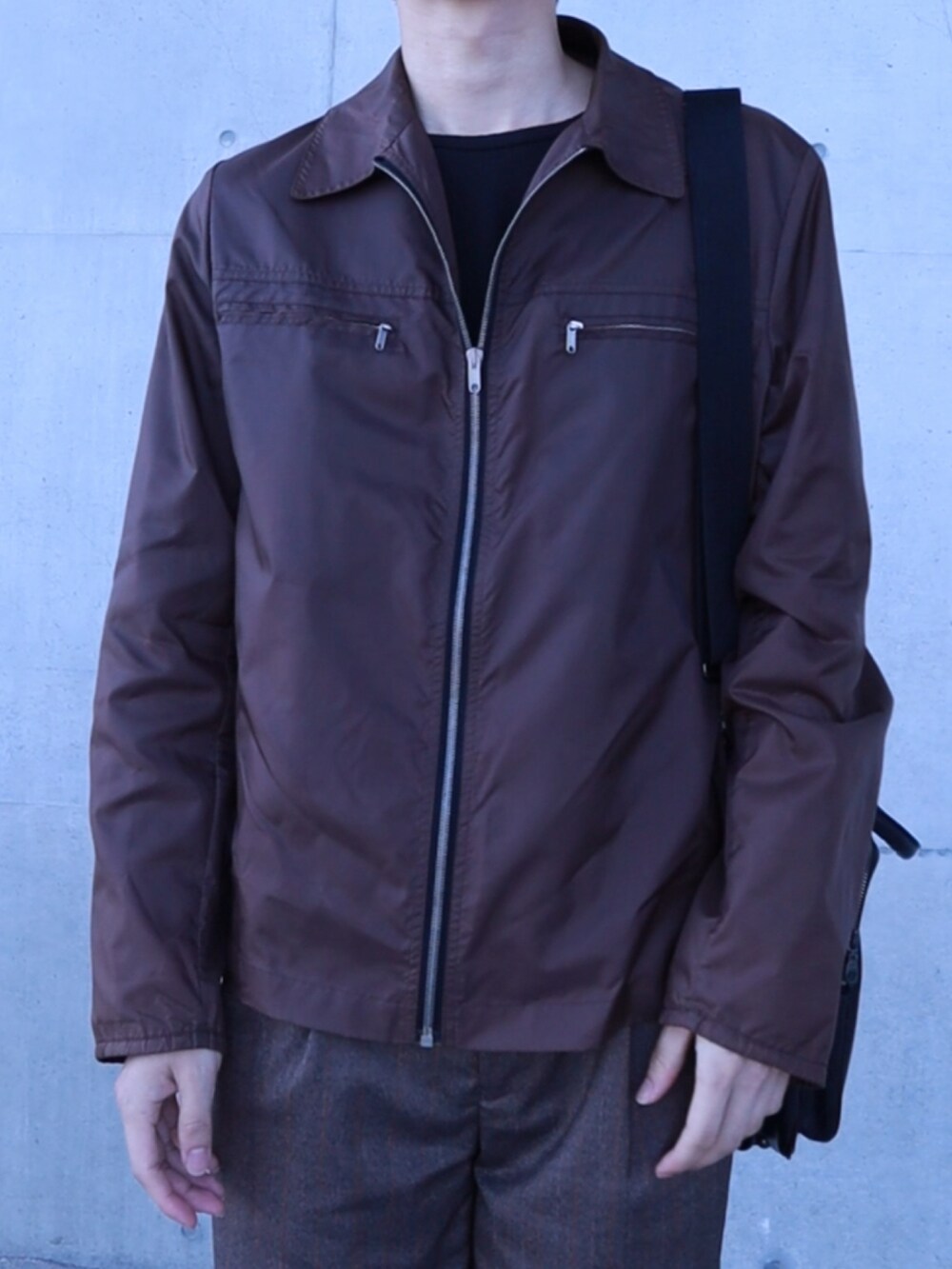 ブラウン系のナイロンジャケット、ブラウン系のスラックス、ブラック系のショルダーバッグを着用したメンズの春コーディネートの2枚目の写真