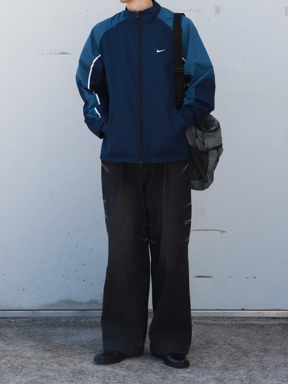 ブルー系のブルゾン、グレー系のショルダーバッグ、ブラック系のデニムパンツを着用したメンズの秋コーディネートの2枚目の写真