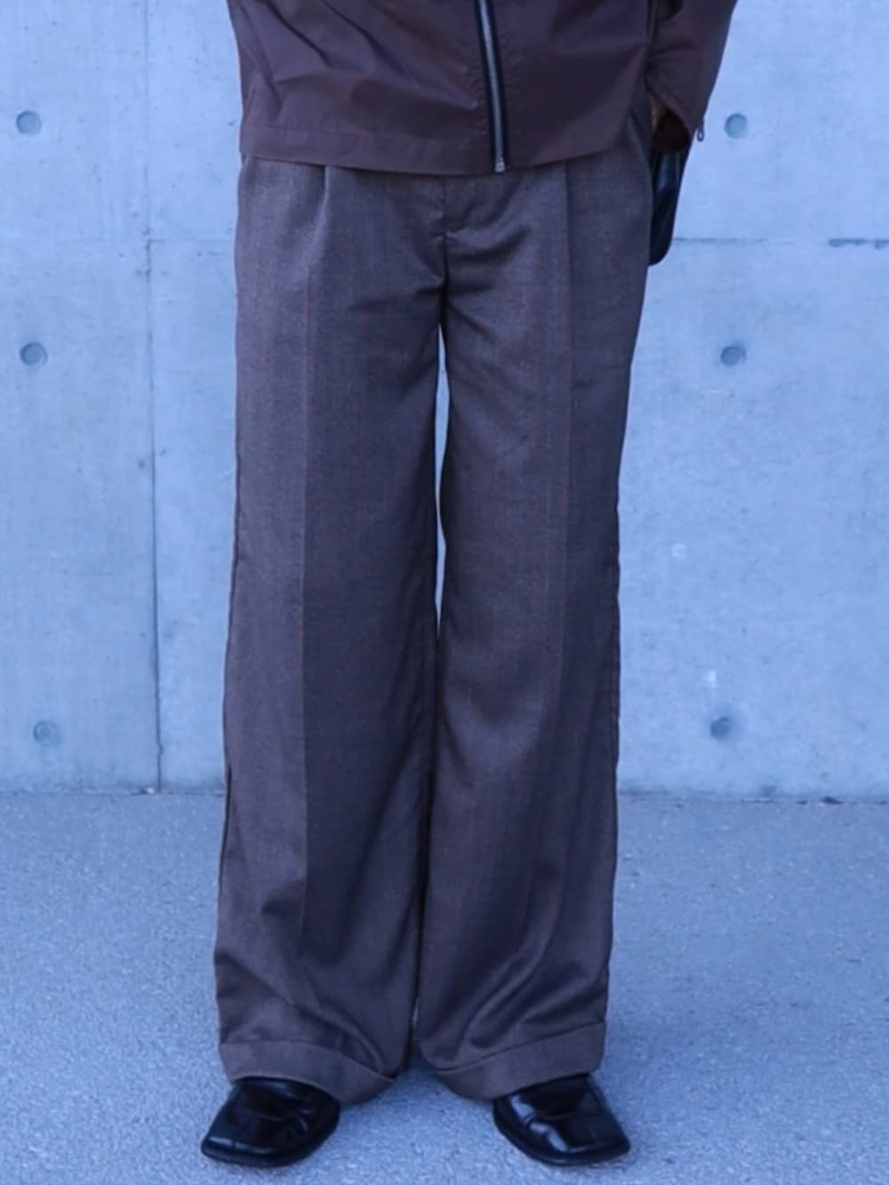 ブラウン系のナイロンジャケット、ブラウン系のスラックス、ブラック系のショルダーバッグを着用したメンズの春コーディネートの4枚目の写真