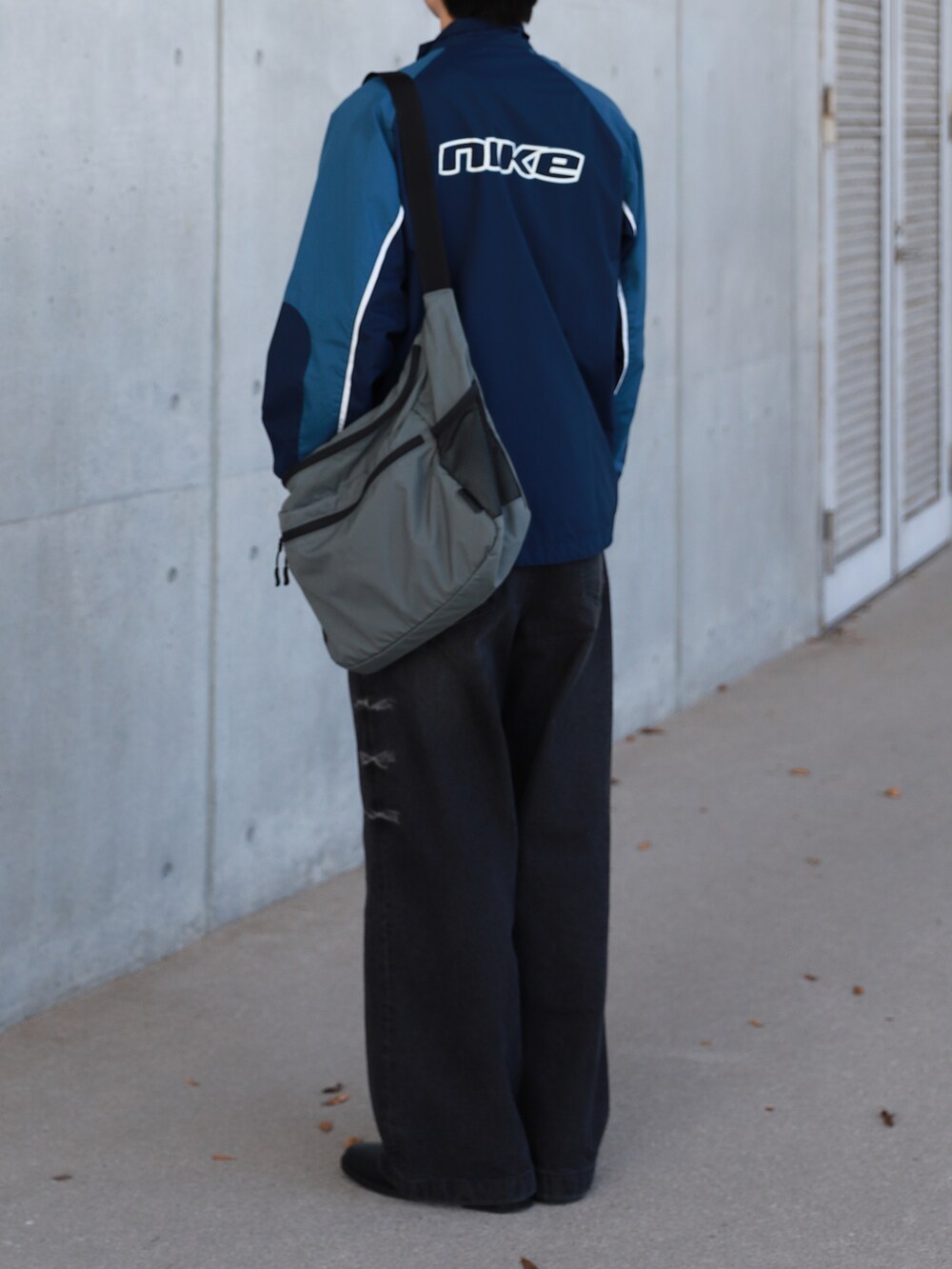 ブルー系のブルゾン、グレー系のショルダーバッグ、ブラック系のデニムパンツを着用したメンズの秋コーディネートの3枚目の写真