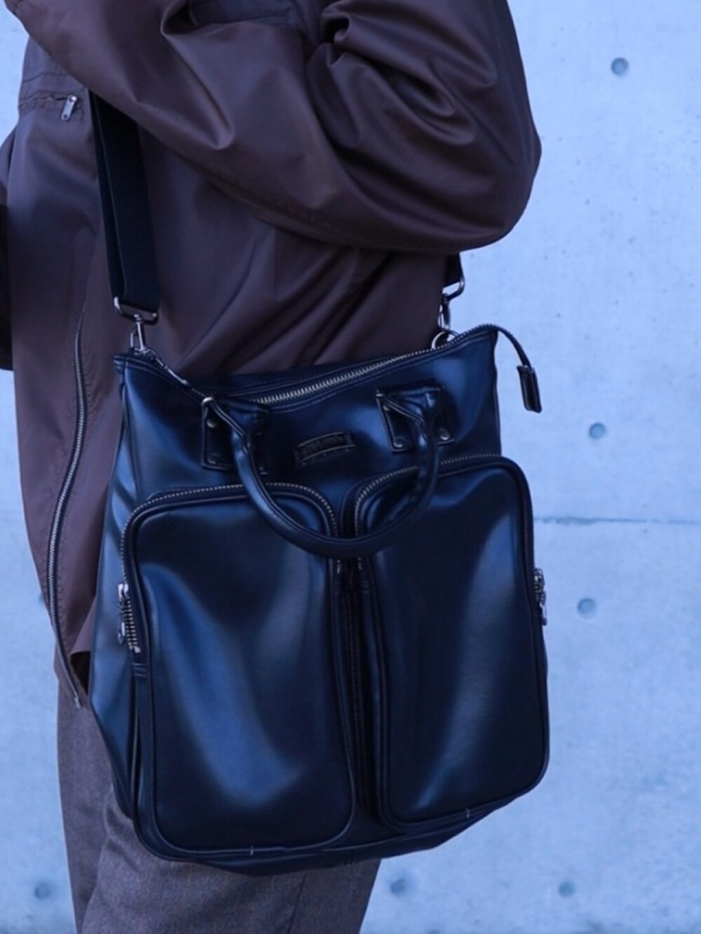 ブラウン系のナイロンジャケット、ブラウン系のスラックス、ブラック系のショルダーバッグを着用したメンズの春コーディネートの3枚目の写真