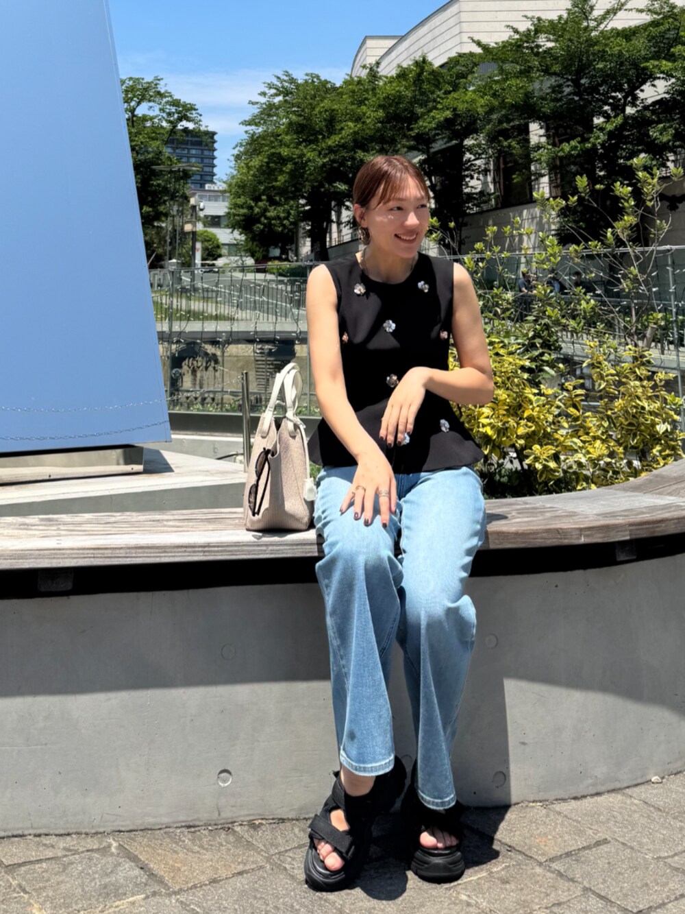 ホワイト系のトートバッグ、ブルー系のデニムパンツ、ブラック系のタンクトップを着用したレディースの夏コーディネートの2枚目の写真