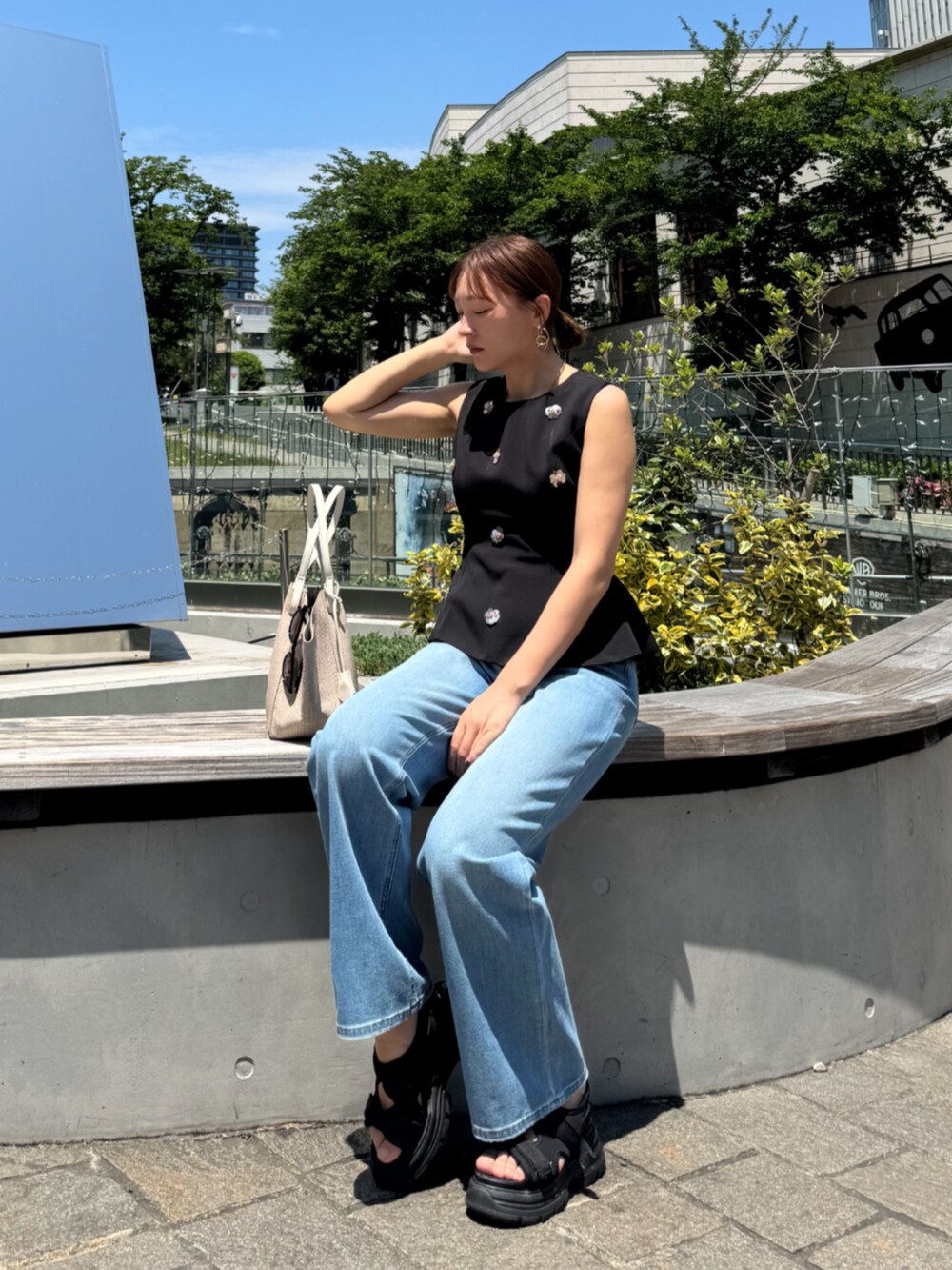 ホワイト系のトートバッグ、ブルー系のデニムパンツ、ブラック系のタンクトップを着用したレディースの夏コーディネートの3枚目の写真