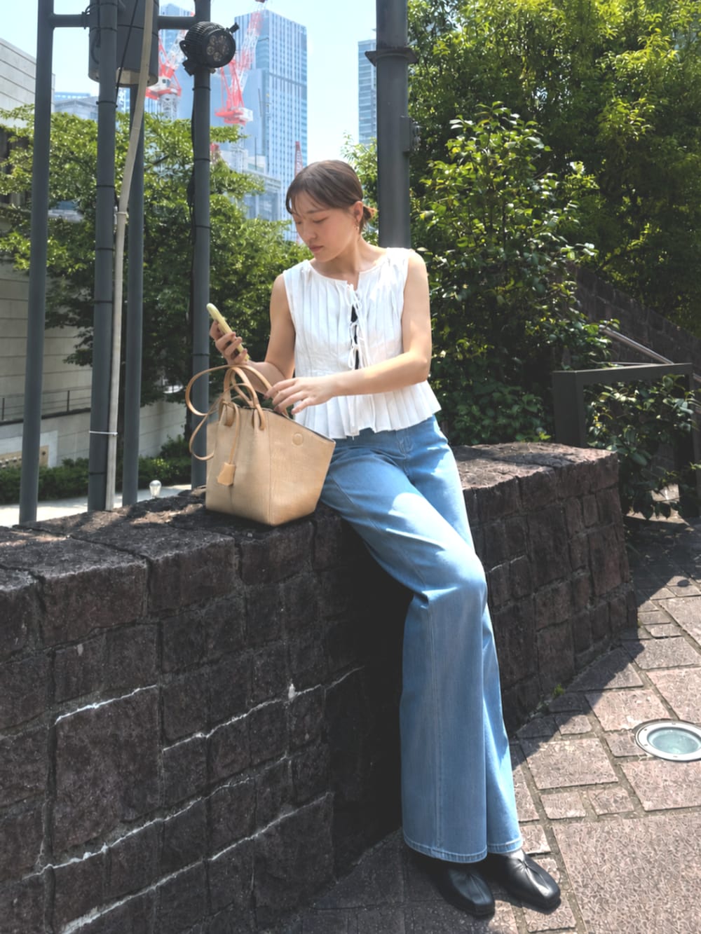ベージュ系のトートバッグ、ブルー系のデニムパンツ、ホワイト系のタンクトップを着用したレディースの夏コーディネートの2枚目の写真