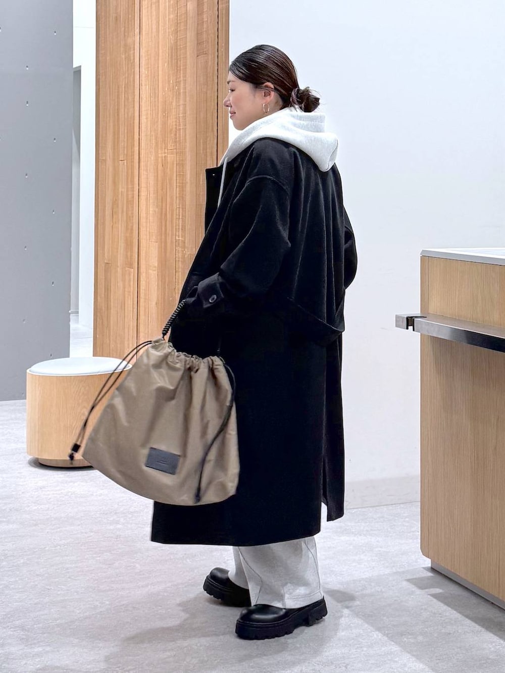 ブラック系のステンカラーコート、グレー系のスウェットパンツ、グレー系のベストを着用したレディースの秋コーディネートの6枚目の写真