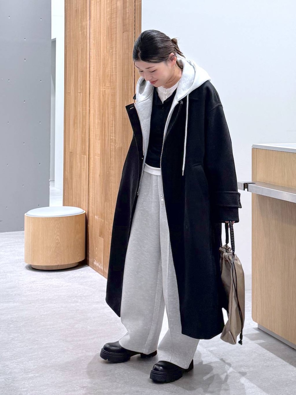 ブラック系のステンカラーコート、グレー系のスウェットパンツ、グレー系のベストを着用したレディースの秋コーディネートの3枚目の写真