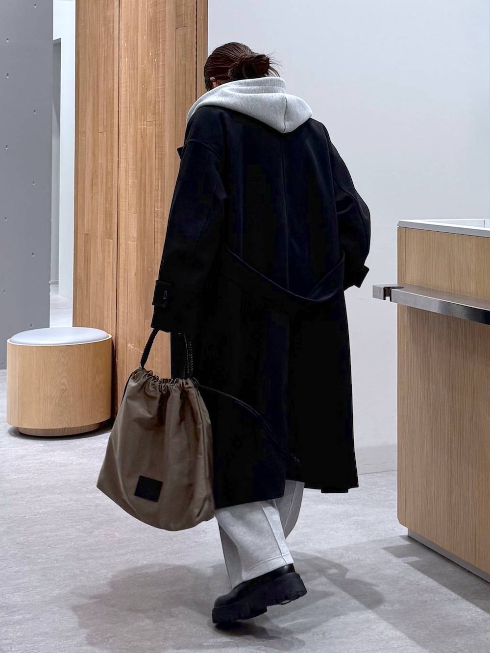 ブラック系のステンカラーコート、グレー系のスウェットパンツ、グレー系のベストを着用したレディースの秋コーディネートの9枚目の写真