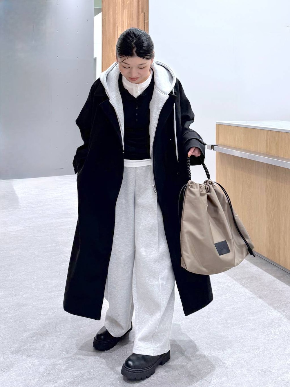 ブラック系のステンカラーコート、グレー系のスウェットパンツ、グレー系のベストを着用したレディースの秋コーディネートの2枚目の写真