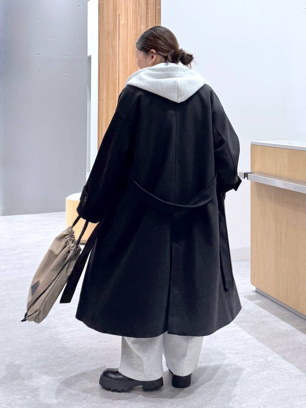 ブラック系のステンカラーコート、グレー系のスウェットパンツ、グレー系のベストを着用したレディースの秋コーディネートの4枚目の写真