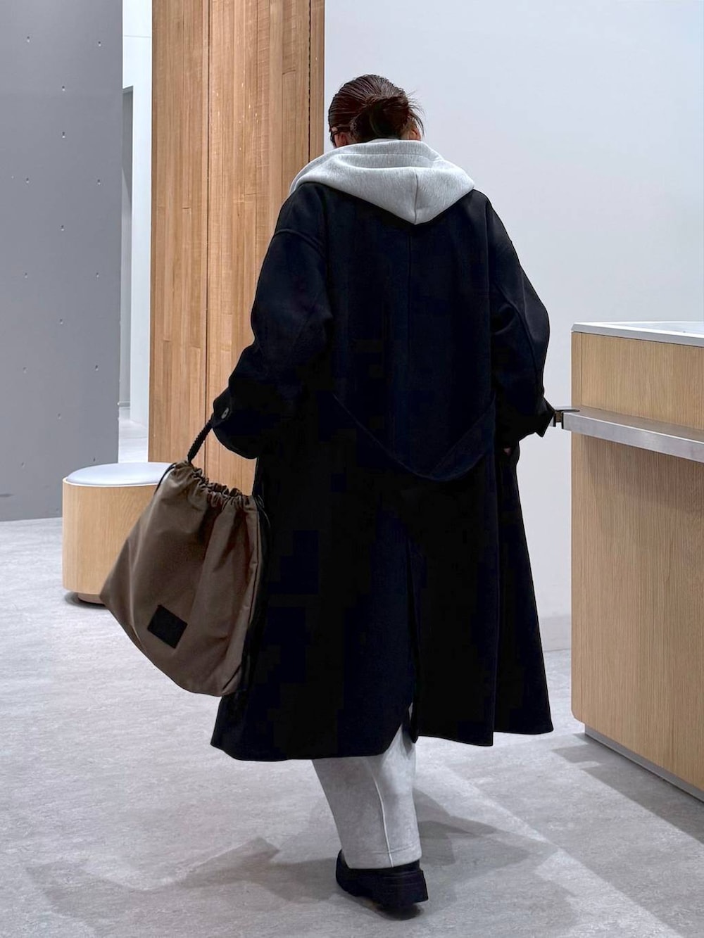 ブラック系のステンカラーコート、グレー系のスウェットパンツ、グレー系のベストを着用したレディースの秋コーディネートの5枚目の写真